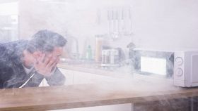 Microonde da cui esce fumo e uomo che guarda