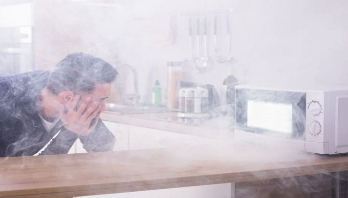 Microonde da cui esce fumo e uomo che guarda