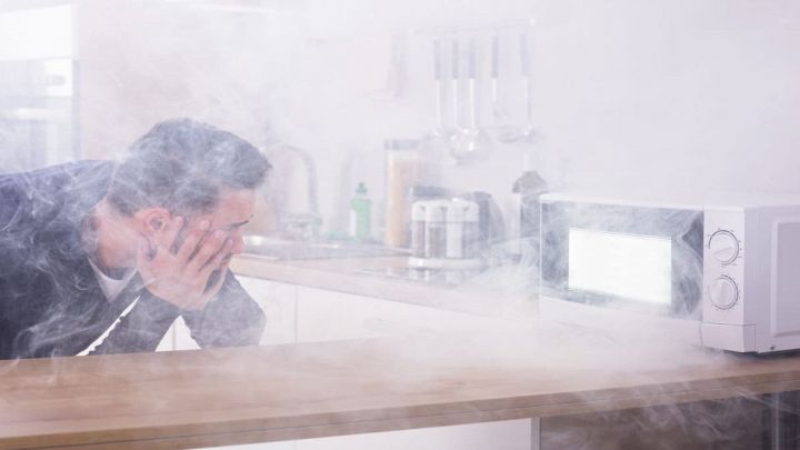 Microonde da cui esce fumo e uomo che guarda