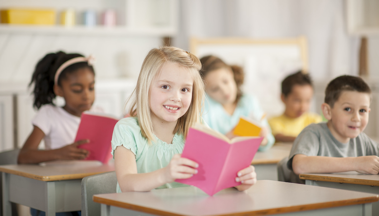 Bambini seduti sui banchi di scuola con il libro in mano