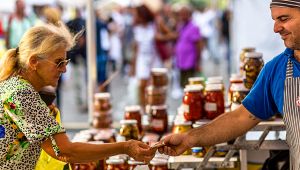 Donna acquista conserve in barattolo da un venditore al banco di una sagra all’aperto affollata