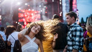Giovani che ballano e sorridono tra la folla davanti a un palco illuminato durante una festa all’aperto