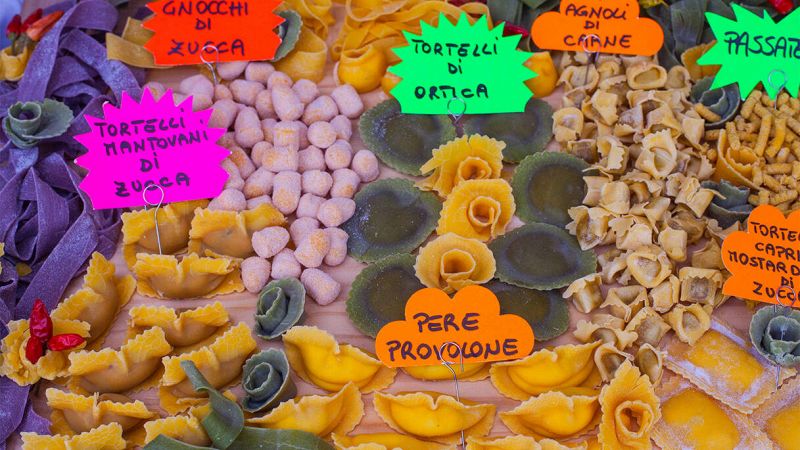 Banco di sagra con vari tipi di pasta fresca ripiena colorata, disposti a gruppi con cartelli scritti a mano