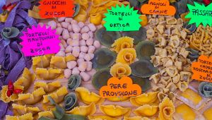 Banco di sagra con vari tipi di pasta fresca ripiena colorata, disposti a gruppi con cartelli scritti a mano