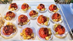 Vassoi con piattini di pomodori al forno ripieni, serviti con patate a tocchetti, esposti su un banco gastronomico