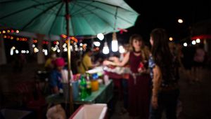 Bancarella notturna a una festa all’aperto con ombrellone verde, luci appese e persone che parlano davanti al chiosco