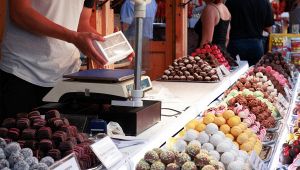 Banco di fiera con vassoi di dolcetti colorati e cioccolatini; venditore pesa una scatola sulla bilancia