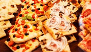 Vassoi con tranci di focaccia e pizza farciti con pomodorini, olive nere, cipolla e funghi esposti su un banco di festa