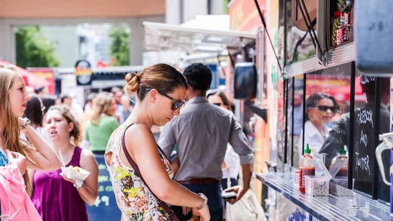 Persone in fila davanti a un colorato food truck all’aperto durante una festa di strada affollata