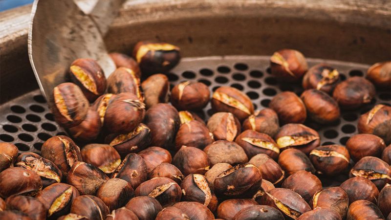 Castagne arrosto in una grande padella forata, rimescolate con una paletta di metallo