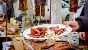 Mano porge un piatto con affettati misti a un banco di salumi in una fiera all’aperto