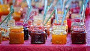 Barattoli di marmellate colorate allineati su un banco, ciascuno con un cucchiaino di metallo inserito