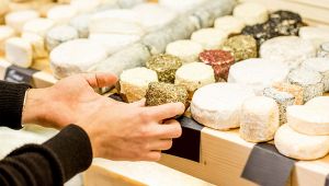 Mani scelgono una piccola forma di formaggio tra molte forme artigianali esposte su un banco di mercato