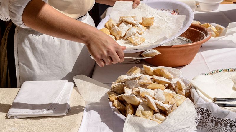Donna in grembiule serve vassoio di dolci fritti ricoperti di zucchero a velo su tavolo imbandito all’aperto