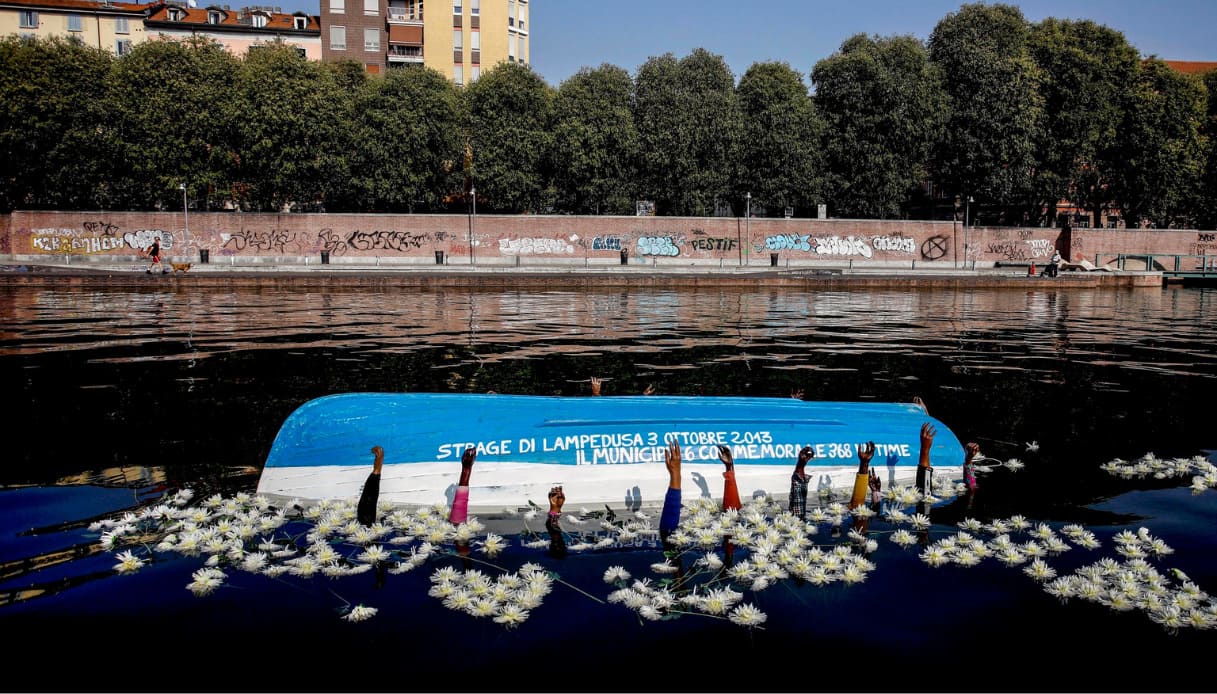 Strage di Lampedusa ricordata a Milano con una barca rovesciata in Darsena: affiorano le braccia dei migranti