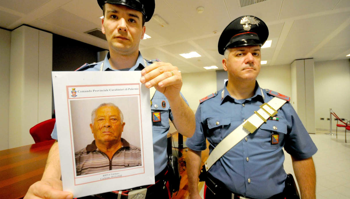 Due carabinieri mostrano la foto segnaletica di Gaetano Riina