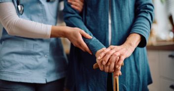Close up of nurse and senior woman with walking cane during home visit.