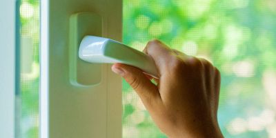 una mano stringe la maniglia di una finestra in pvc