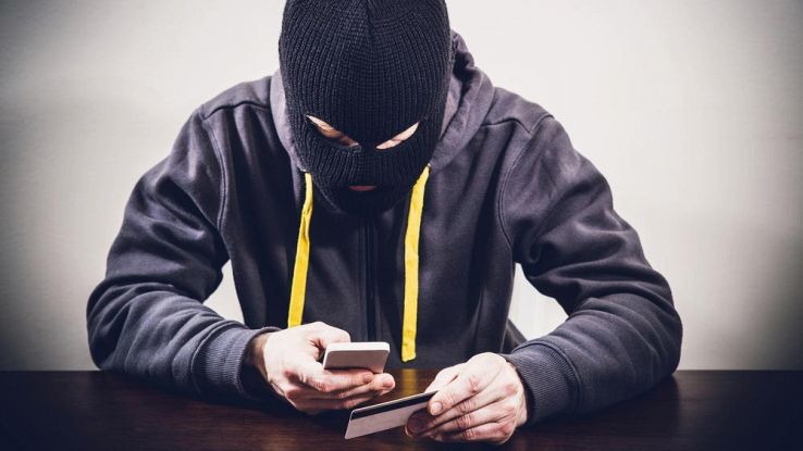 Un uomo incappucciato tiene in mano uno smartphone e una carta di credito