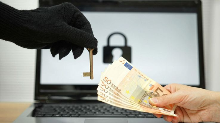 Una mano con un guanto porge una chiave a un'altra mano che porge dei contanti, nello sfondo un PC con l'immagine di un lucchetto