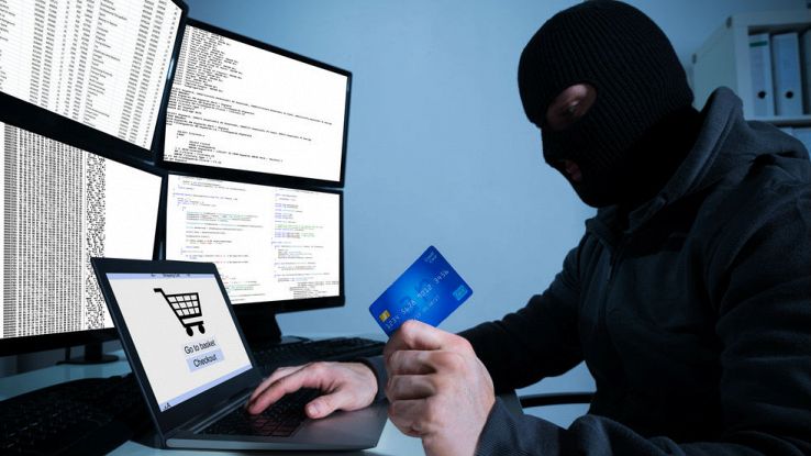 Un uomo incappucciato tiene in mano una carta di credito mentre manomette un PC