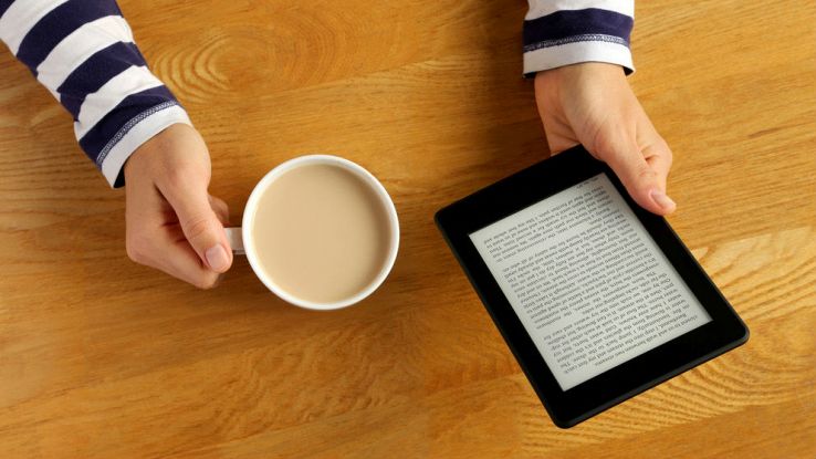 Una donna legge dal suo Kindle mentre beve una tazza di caffè