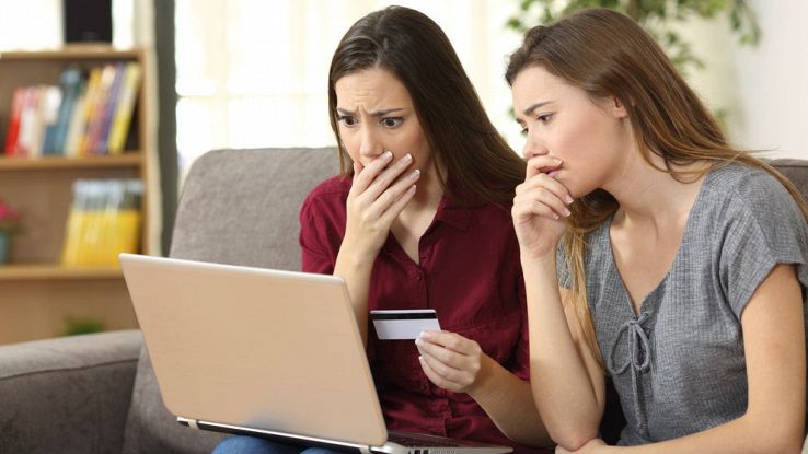 Due ragazze si spaventano guardando un computer mentre tengono una carta di credito in mano