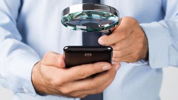 uomo con lente d'ingrandimento spia uno smartphone