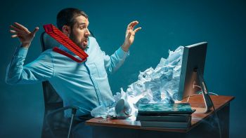 Un uomo sommerso da cartacce di fronte al computer