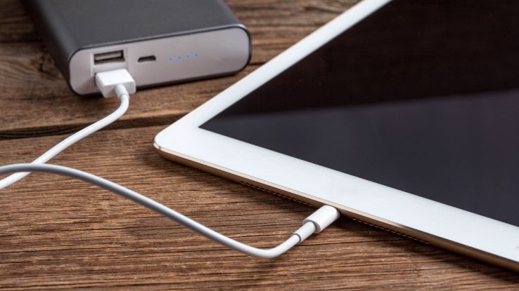 Power bank 20.000 mAh in offerta oggi che ricarica uno smartphone tramite cavo su tavolo in legno