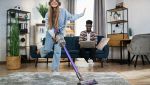 Donna che usa una scopa elettrica senza fili per pulire il tappeto in salotto.