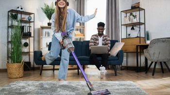 Donna che usa una scopa elettrica senza fili per pulire il tappeto in salotto.