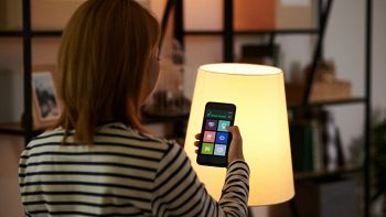 Controllo luci smart con smartphone davanti a una lampada accesa.