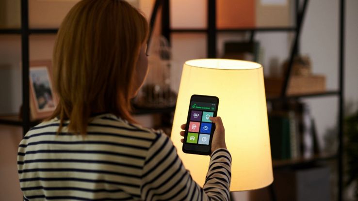 Controllo luci smart con smartphone davanti a una lampada accesa.