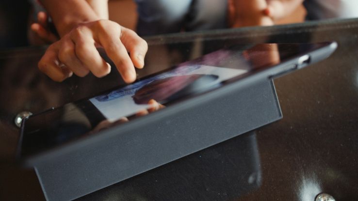 Bambino che tocca lo schermo di un tablet appoggiato a un supporto.