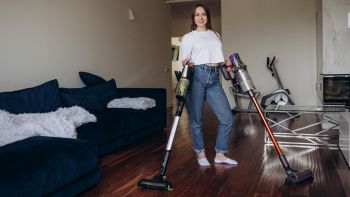 Donna con due aspirapolvere senza fili mentre pulisce il soggiorno; focus su modelli tipo Dyson e Rowenta in promozione.