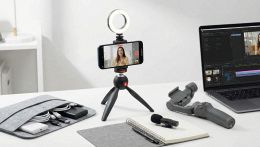 Smartphone montato su treppiede con ring light accesa e microfono esterno, posizionato su una scrivania moderna da content creator.