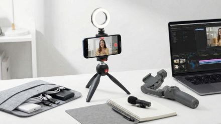 Smartphone montato su treppiede con ring light accesa e microfono esterno, posizionato su una scrivania moderna da content creator.