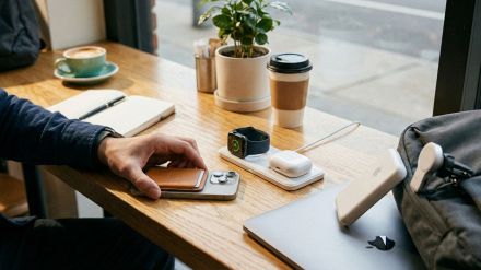 Setup da scrivania moderno con iPhone su stand di ricarica MagSafe 3-in-1, portafoglio magnetico in pelle, custodia AirPods e power bank wireless in stile minimal tech
