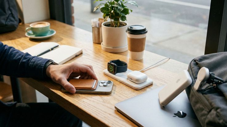 Setup da scrivania moderno con iPhone su stand di ricarica MagSafe 3-in-1, portafoglio magnetico in pelle, custodia AirPods e power bank wireless in stile minimal tech