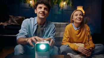 Coppia guarda un film con mini proiettore portatile Full HD collegato in Wi-Fi; uso domestico in salotto.