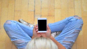 Ragazza con smartphone seduta sul pavimento