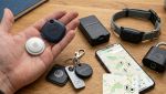 Mano con Apple AirTag e Samsung SmartTag accanto a Tile e Chipolo, smartphone con mappa e accessori antifurto smart.