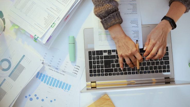 Una donna utilizza un computer circondata di fogli e grafici