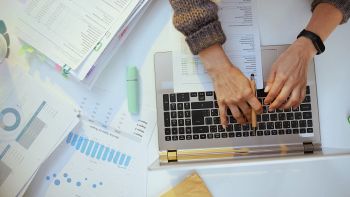 Una donna utilizza un computer circondata di fogli e grafici