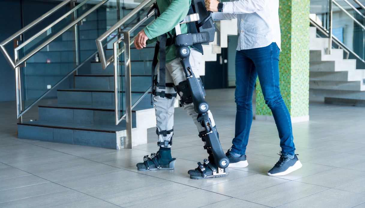 https://wips.plug.it/cips/tecnologia/cms/2026/03/persona-con-esoscheletro-meccanico-sostenuta-da-un-altra.jpg