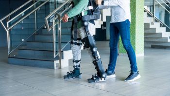 Esoscheletro meccanico indossato da persona sorretta da un’altra