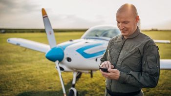 Un pilota fermo di fronte al suo aeroplano con uno smartphone in mano