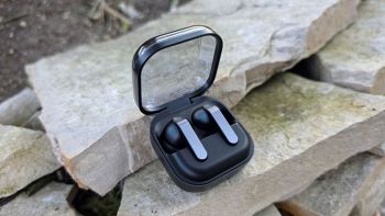 Alt-text: Samsung Galaxy Buds 4 Pro nella custodia aperta con coperchio trasparente su sfondo di pietre