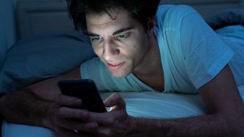 Ragazzo con smartphone a letto e luce blu
